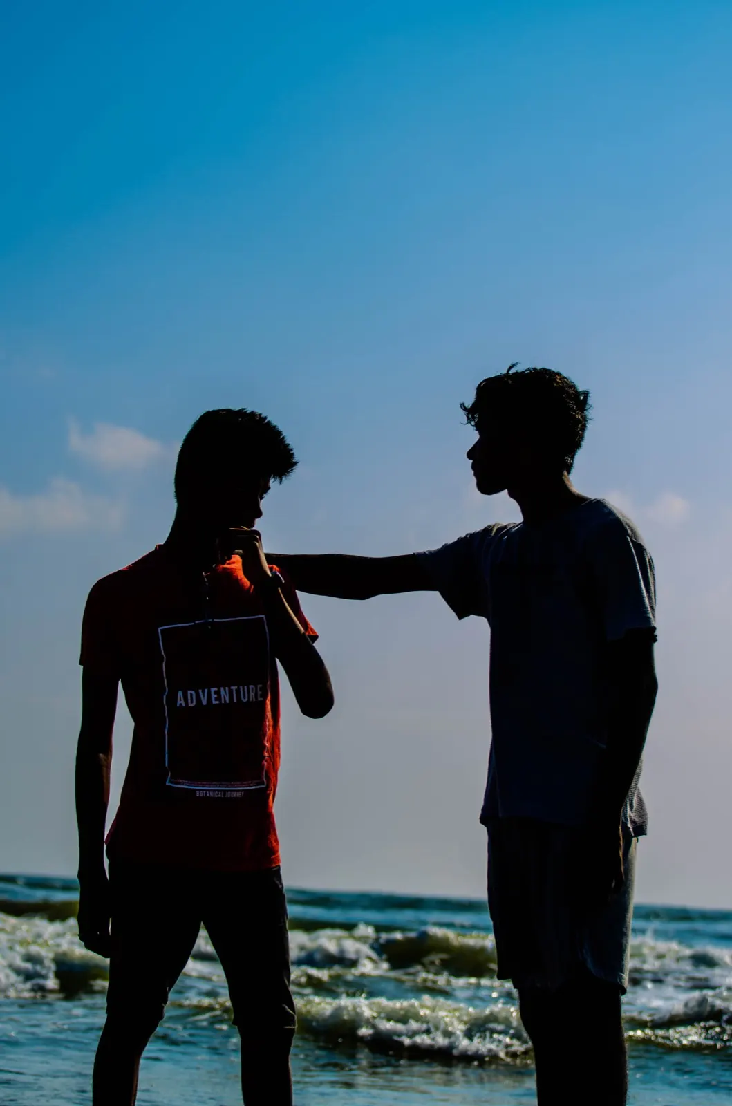 Silhouette of two friends against a deep blue sky at the beach