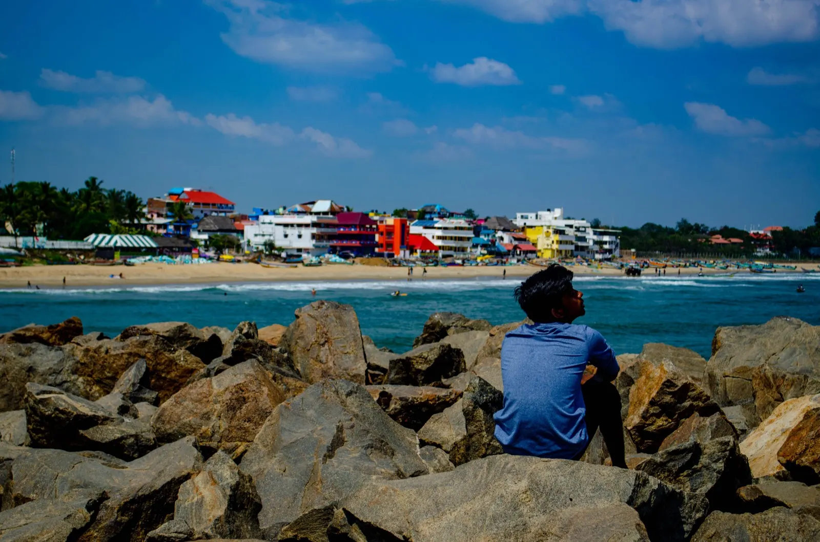 Man sitting on breakwater rocks looking at a colourful coastal town and beach