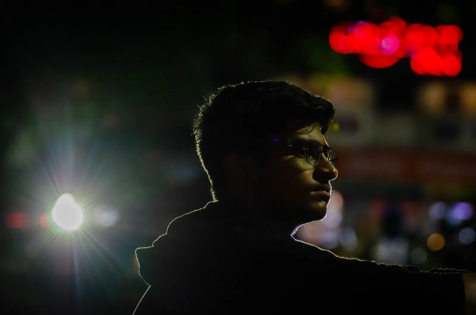 Rim-lit night portrait with a bright street light flare and red neon bokeh