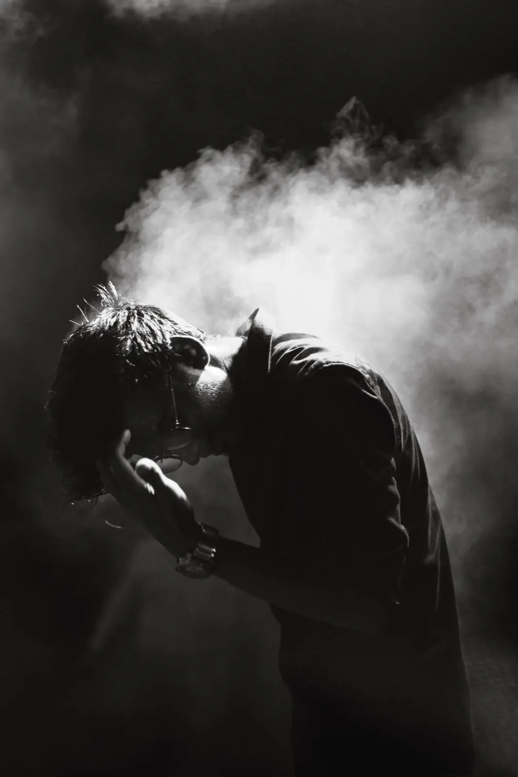 Black and white photo of a guitarist bowed forward in stage smoke