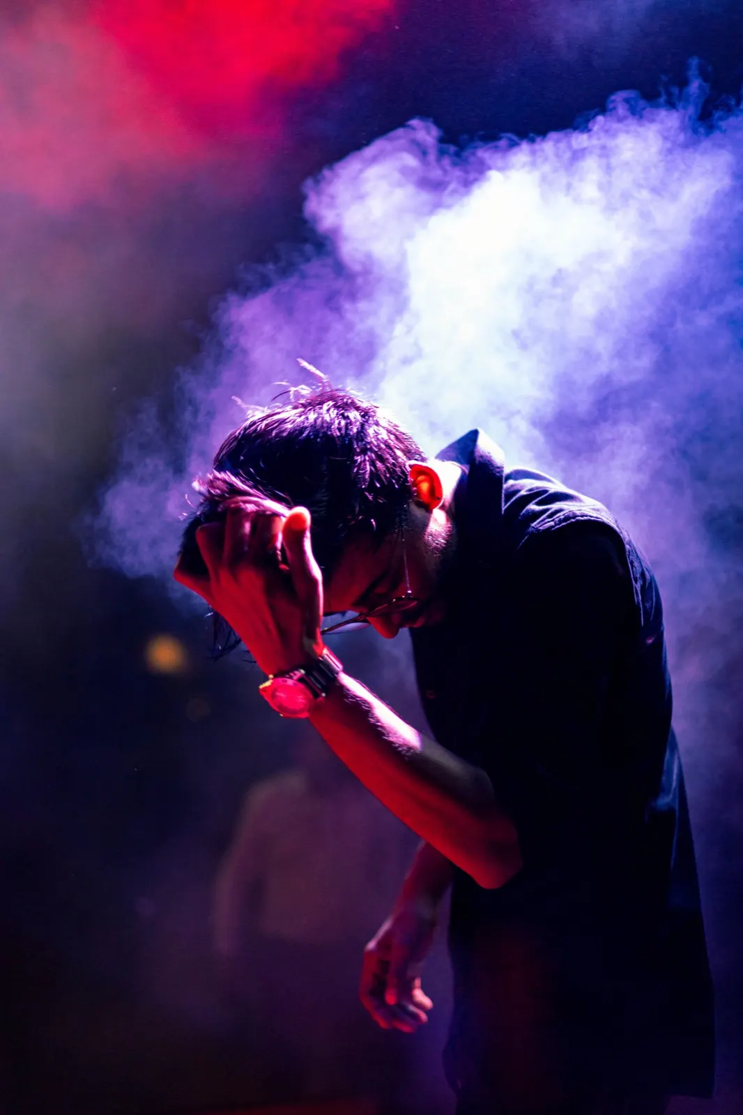 Guitarist head bowed under red and blue stage smoke