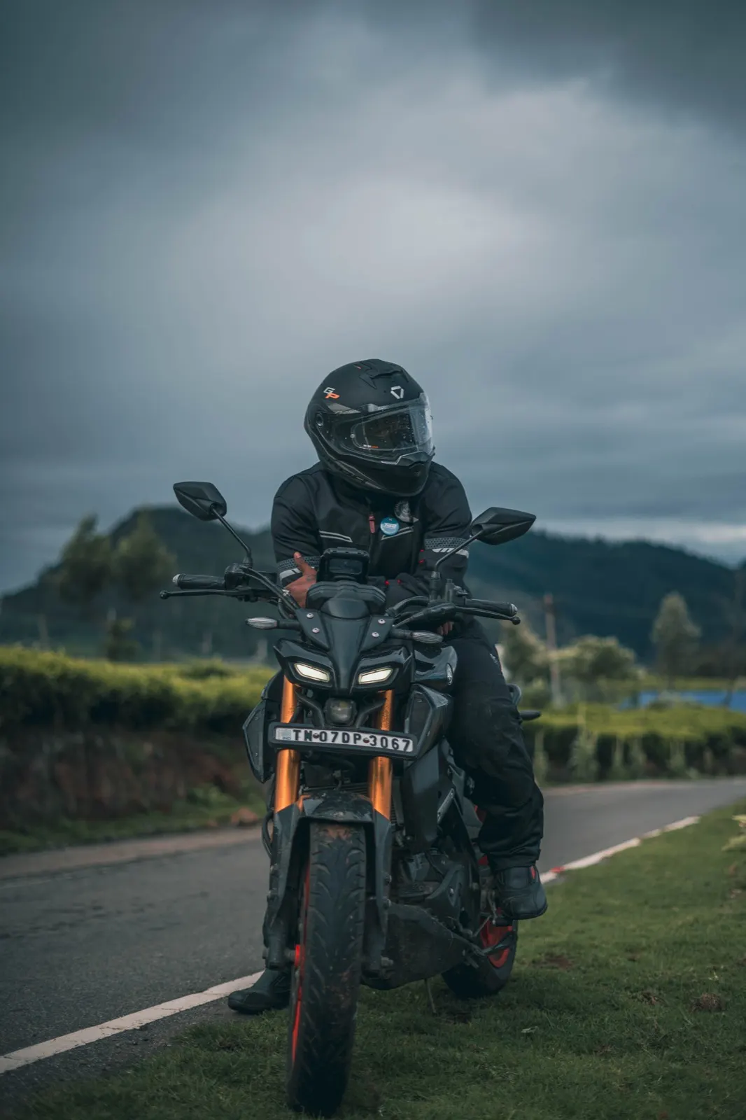 Helmeted rider astride a motorcycle with glowing daytime running lights under a heavy storm sky