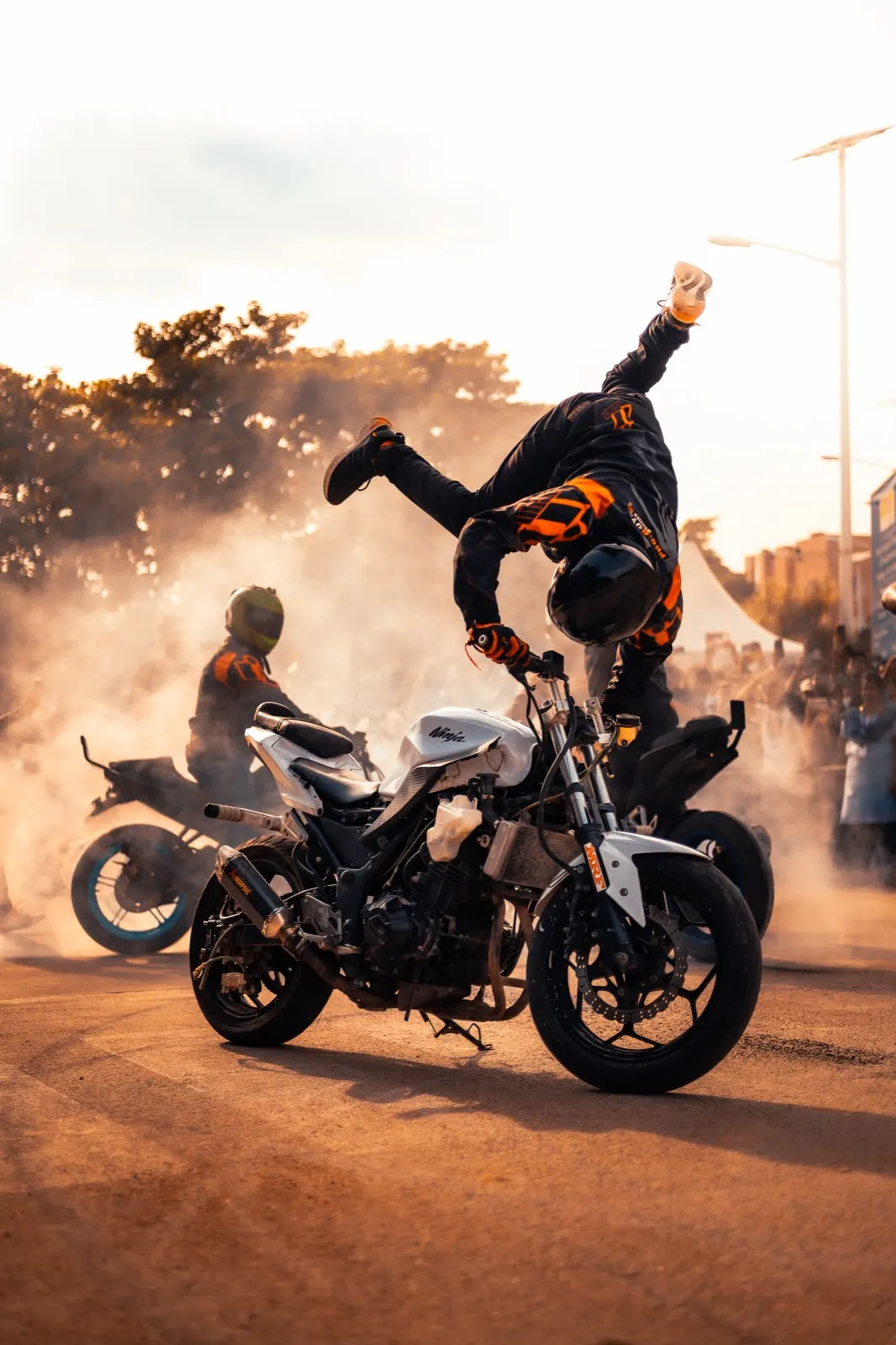 Stunt rider doing a handstand on a moving motorcycle through golden dust