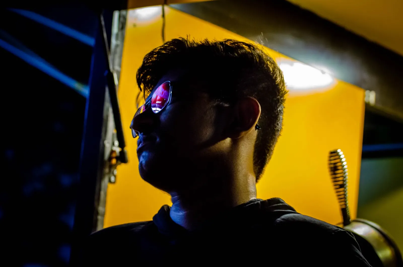 Profile portrait lit by a yellow wall of light, sunglasses reflecting pink